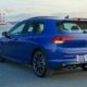 A blue car drives by the coast.