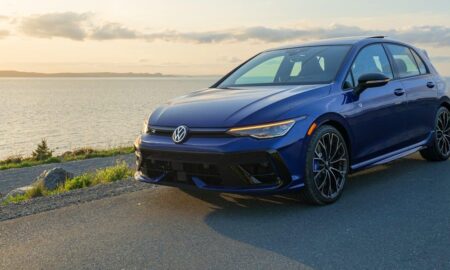 A blue car parked near the ocean at sunset.