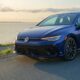 A blue car parked near the ocean at sunset.