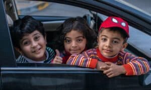 three boys looking outside window of car front seat