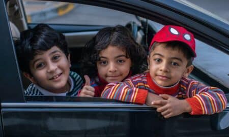 three boys looking outside window of car front seat