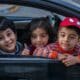 three boys looking outside window of car front seat
