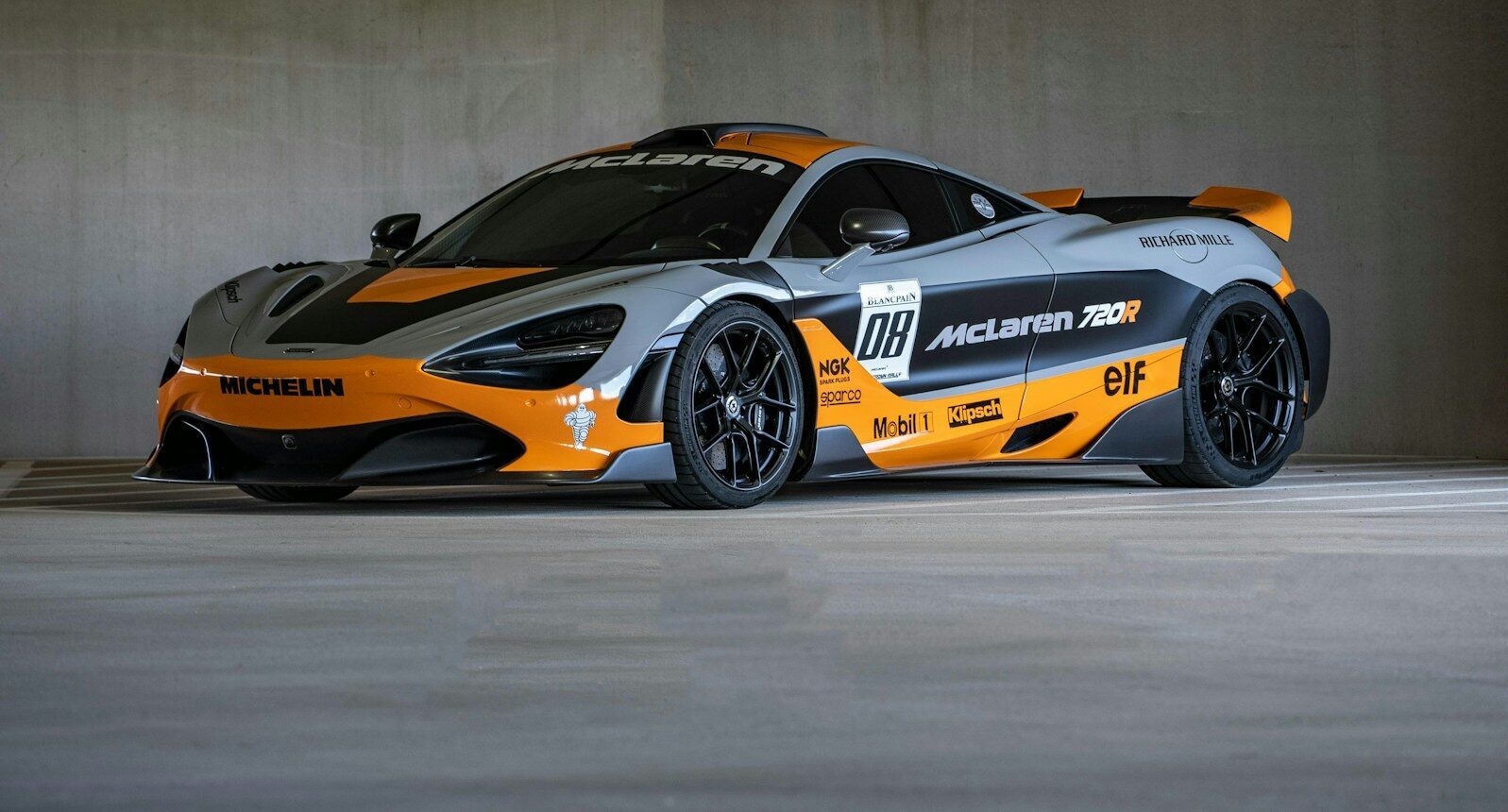 A grey and orange mclaren race car parked indoors