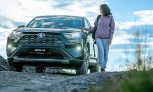 A woman standing next to a car on a dirt road