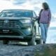 A woman standing next to a car on a dirt road
