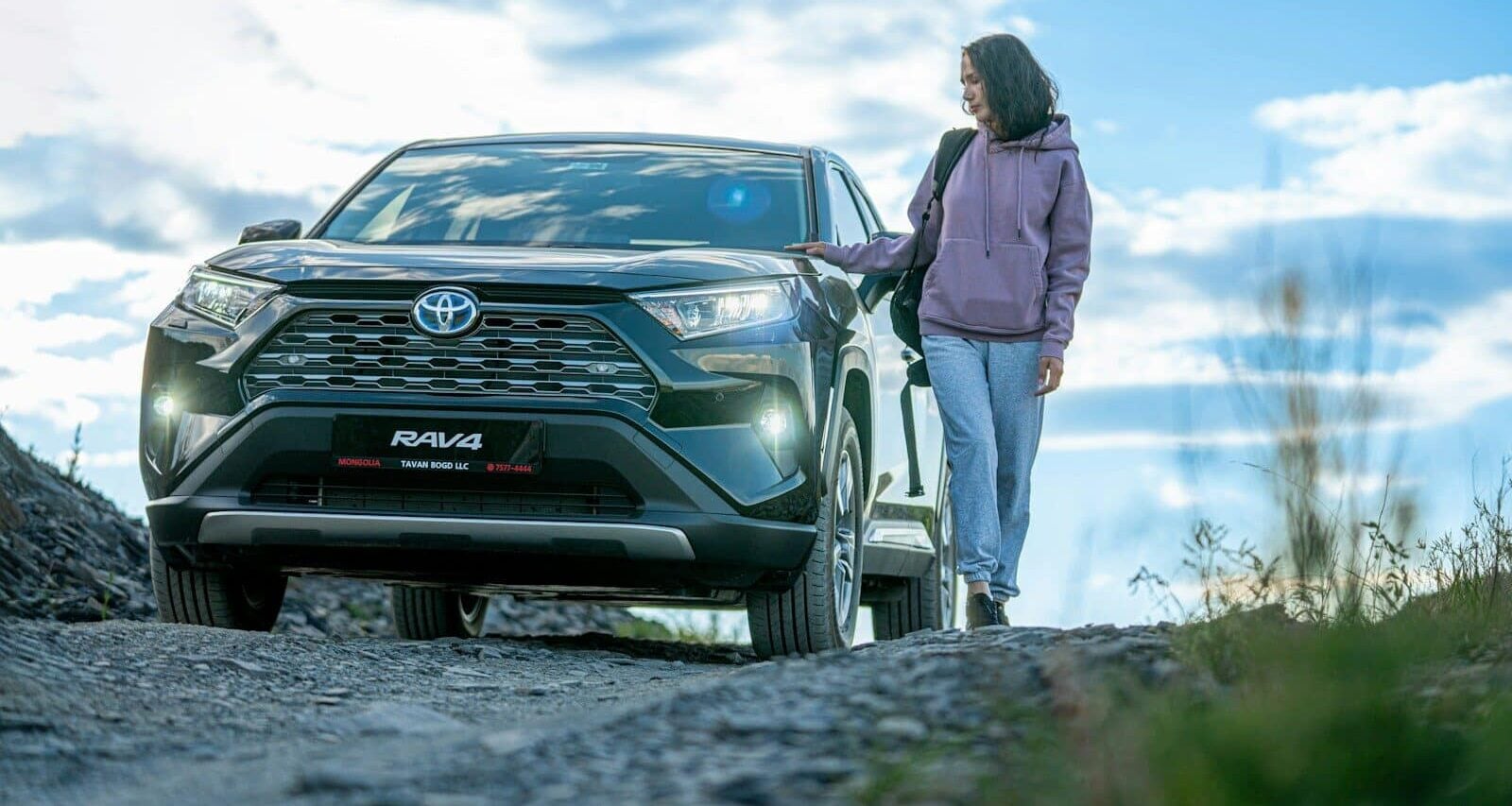 A woman standing next to a car on a dirt road