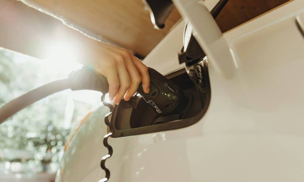 A hand plugging a charging cable into a white electric vehicle