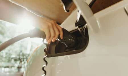 A hand plugging a charging cable into a white electric vehicle