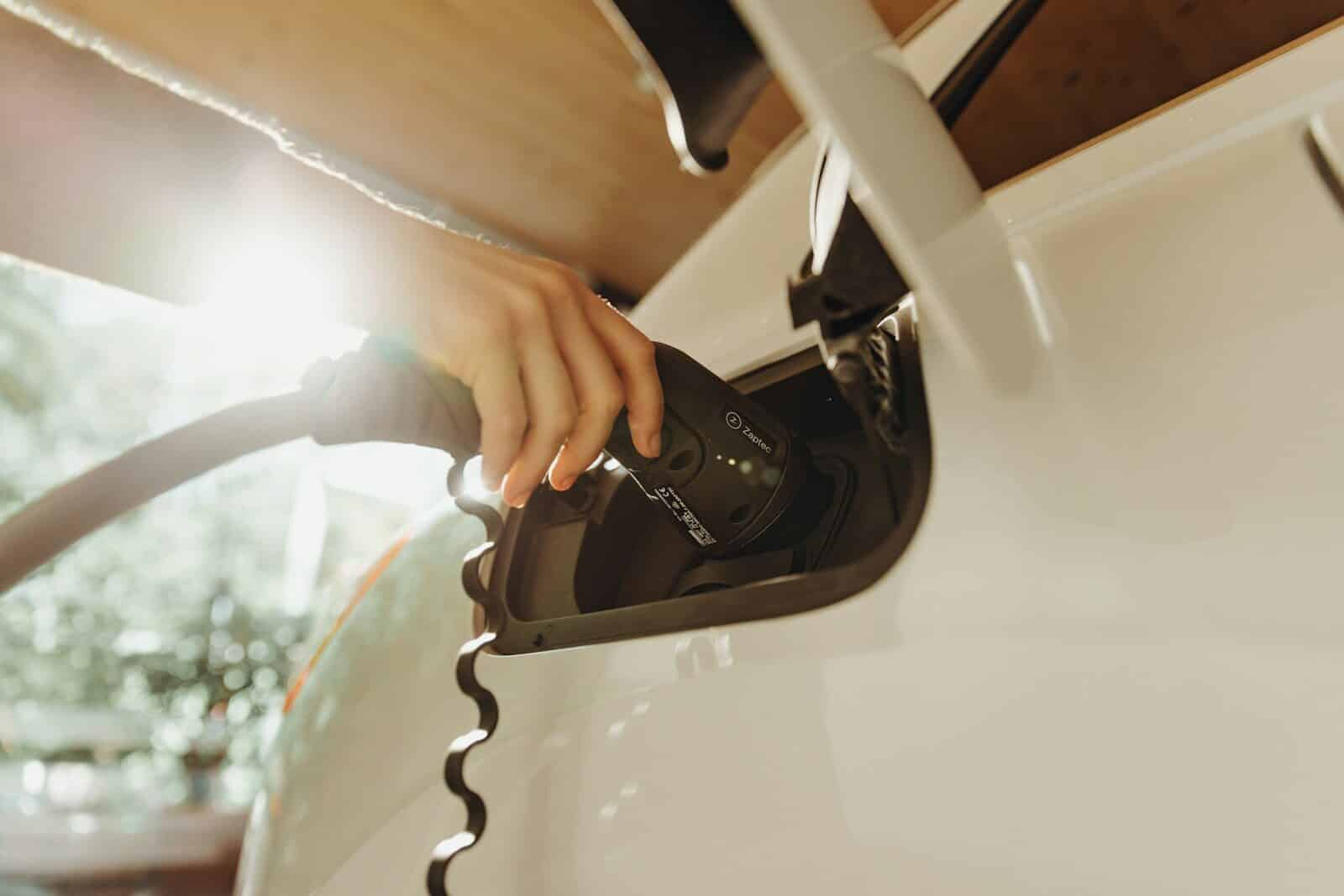 A hand plugging a charging cable into a white electric vehicle