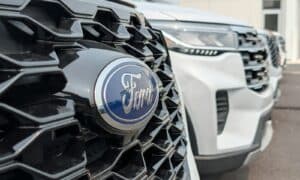 A Ford emblem on a black honeycomb grille with white vehicles parked behind