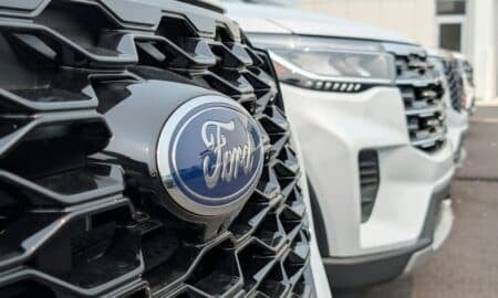 A Ford emblem on a black honeycomb grille with white vehicles parked behind