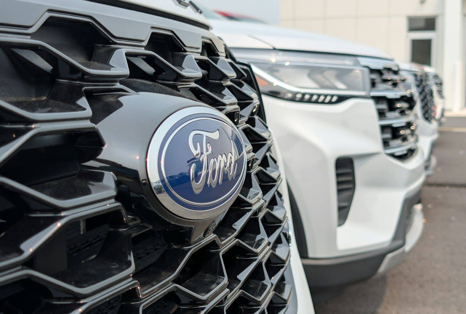 A Ford emblem on a black honeycomb grille with white vehicles parked behind