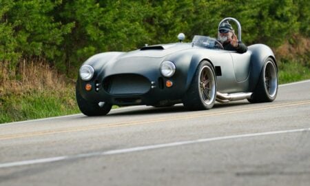 A dark gray vintage sports car driving on a road.