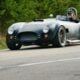 A dark gray vintage sports car driving on a road.