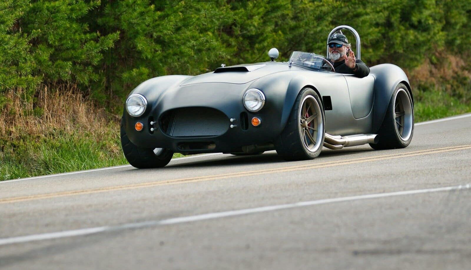 A dark gray vintage sports car driving on a road.